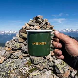 The same mug in a hiker's hand at a summit cairn